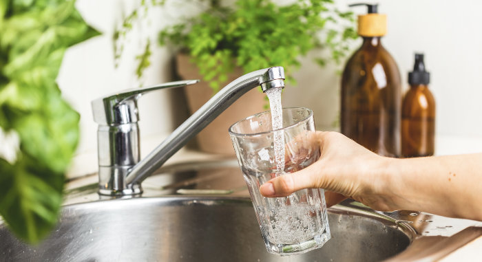 Female hand holding a glass and pouring it with tap water in the kitchen at home. Stay hydrated and filtering water concept. World water day